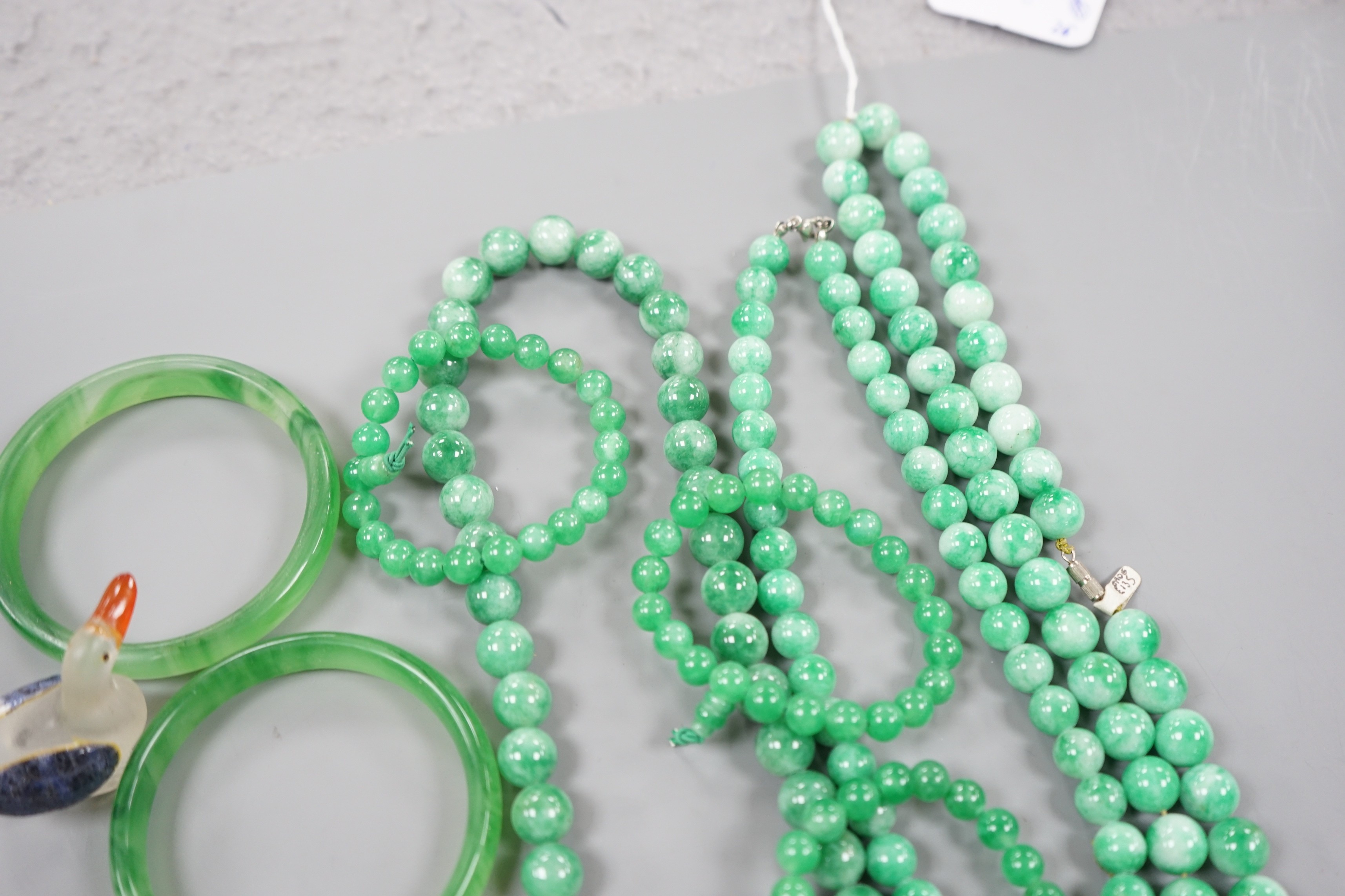 A group of three jadeite necklaces, together with two jadeite bracelets, two green glass bangles and a glass figure of a duck (8)